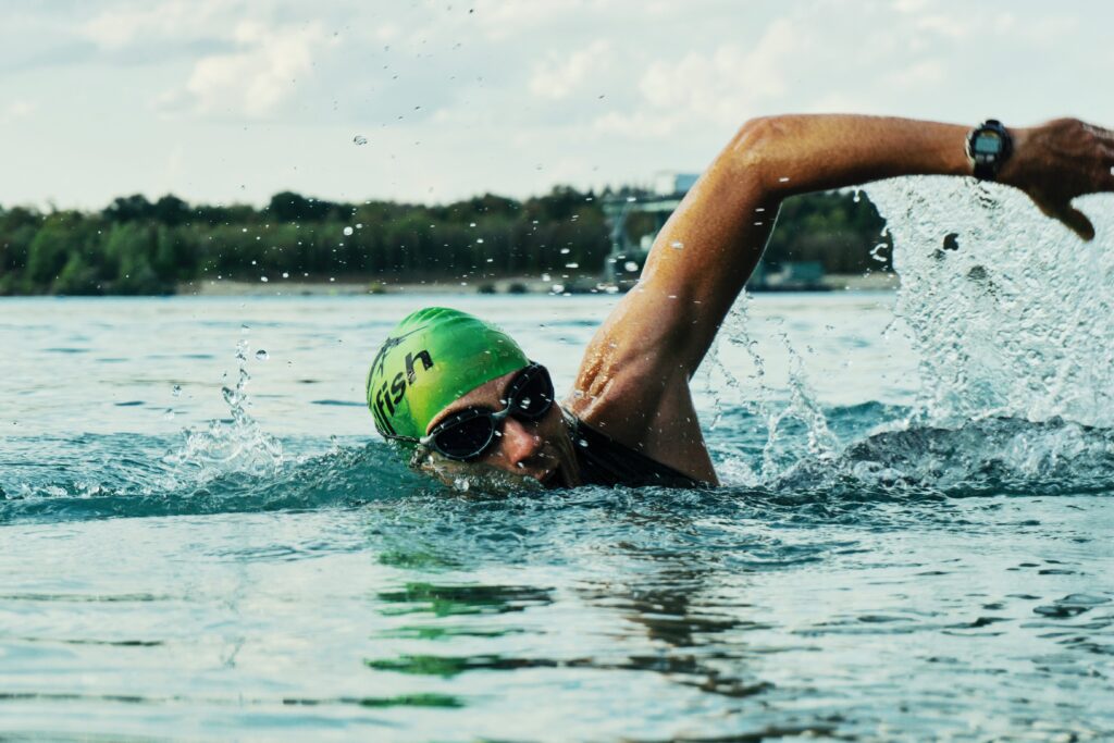 緑の競泳キャップをかぶった男性がクロールで泳いでいる写真